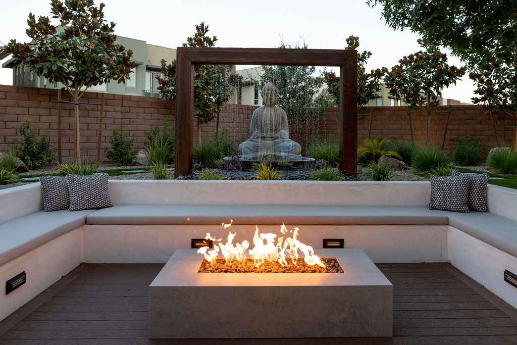 A backyard scene featuring a fire pit, a wooden bench, and a calming Buddha statue, perfect for outdoor gatherings.