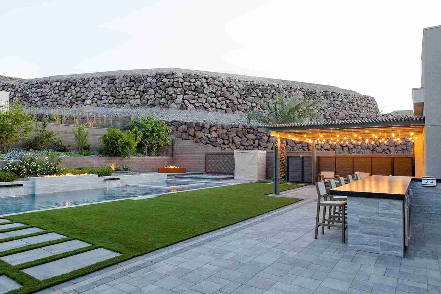 A backyard featuring a pool, outdoor dining area, and lush turf surrounding the space.